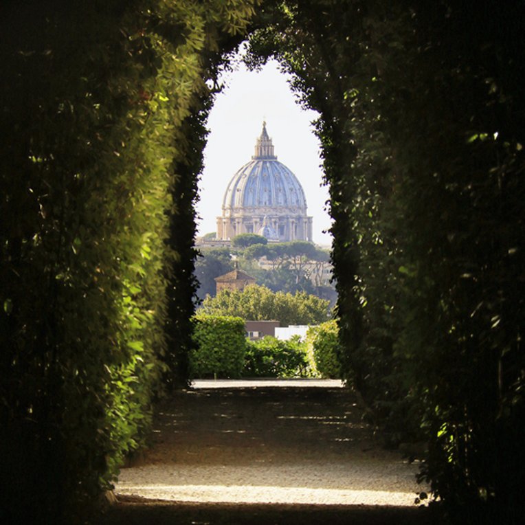 Blick auf eine Kirche, die durch einen Tunnel aus Bäumen sichtbar wird, inspiriert von Rom Versteckte Blick.