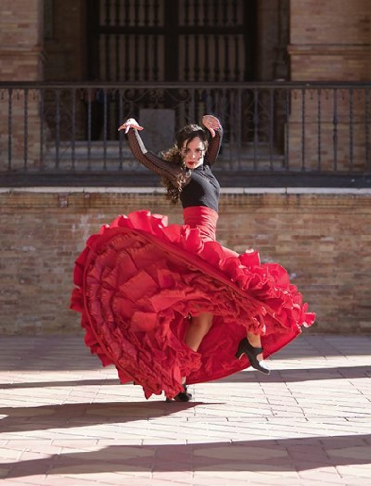 Eine Frau in einem roten Rock tanzt vor einem Gebäude in Spanien.