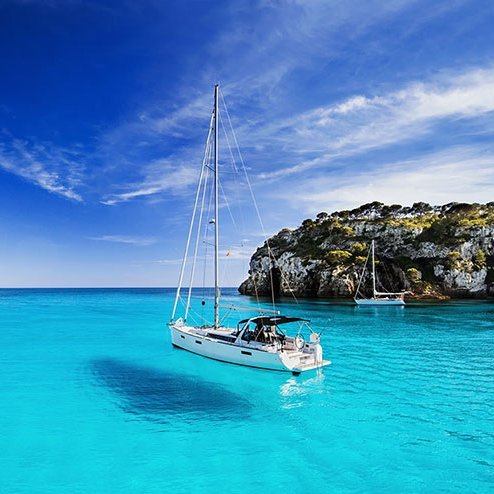 Ein Segelboot schaukelt sanft im klaren blauen Wasser vor der Küste von Menorca.