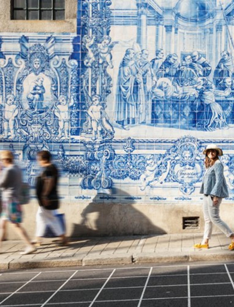 Eine Frau spaziert auf der Straße, während die Sonne scheint und Passanten vorbeigehen.