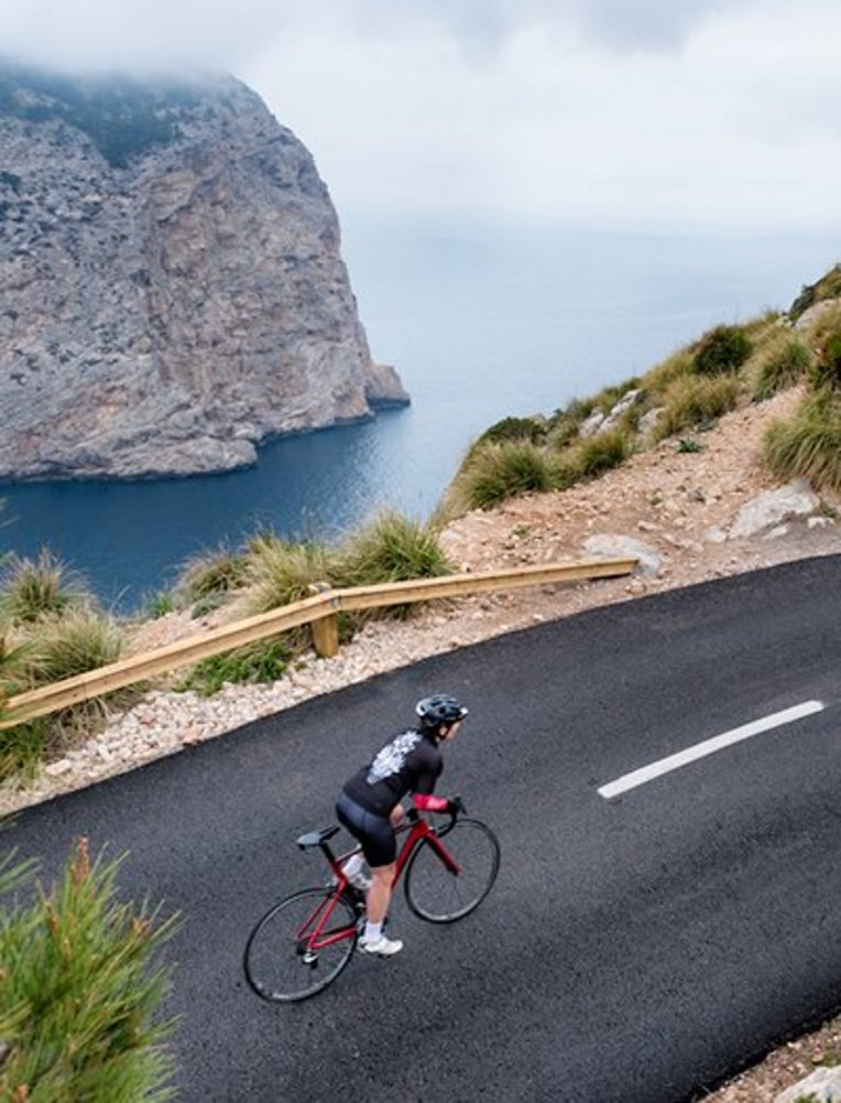 Ein Mann fährt mit dem Fahrrad auf einer Straße in Mallorca, umgeben von der schönen Landschaft der Insel.