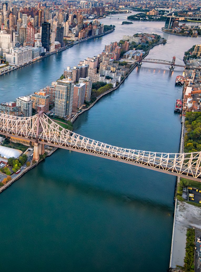 Eine Brücke über ein Gewässer in New York City, umgeben von urbaner Landschaft und Wolkenkratzern.