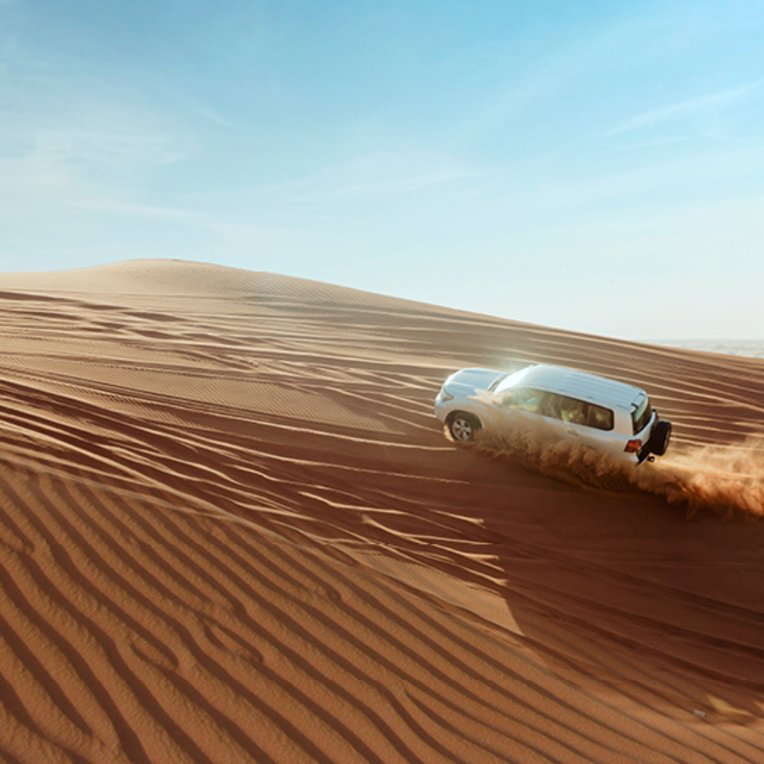  Ein weisser SUV fährt durch die Wüste in Dubai.