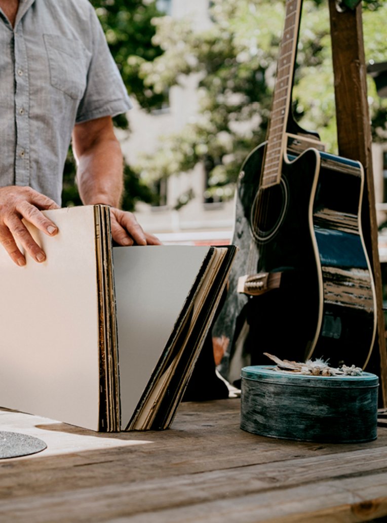 Ein Mann in Berlin hält eine Gitarre und einen Stapel Schallplatten in der Hand.