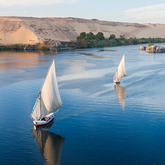 Zwei Segelboote auf dem Nil in Ägypten, umgeben von sanften Wellen und der malerischen Landschaft.