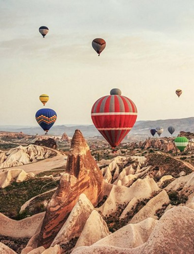 Viele Heissluftballons schweben über die felsige Landschaft von Kappadokien.