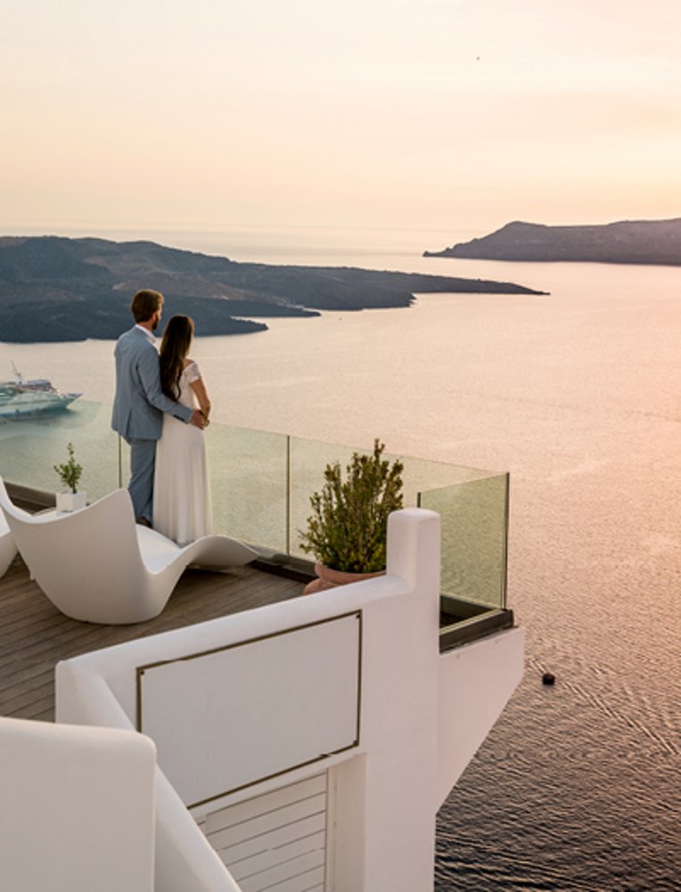 Ein Paar steht auf einem Balkon und blickt auf das Meer, umgeben von der romantischen Atmosphäre der griechischen Inseln.