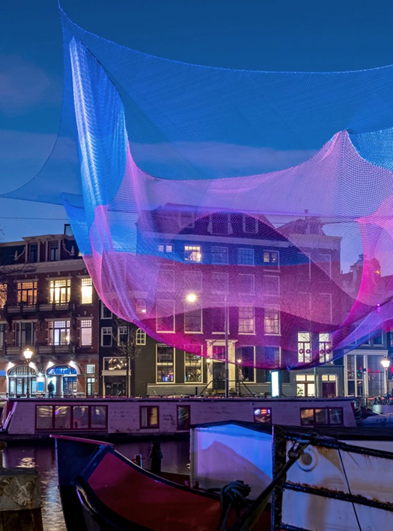 Ein Boot liegt am Dock vor einem Gebäude in Amsterdam, das mit einem Netz überzogen ist.