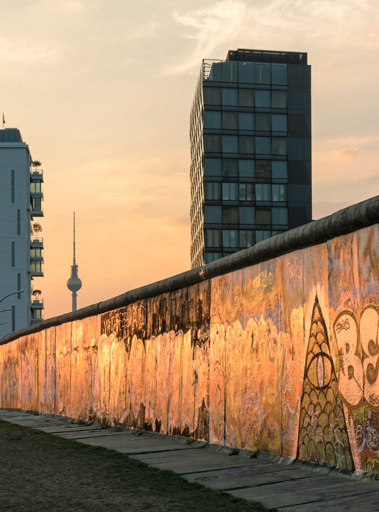 Die Berliner Mauer bei Sonnenuntergang, mit warmen Farben, die den Himmel und die Mauer beleuchten.