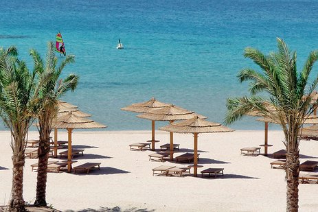 Sandstrand mit Palmen, Strohdächern und türkisfarbenem Meer.