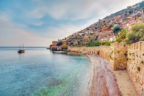 Türkische Küste mit Sandstrand, Palmen, Strohdächern und türkisfarbenem Meer.