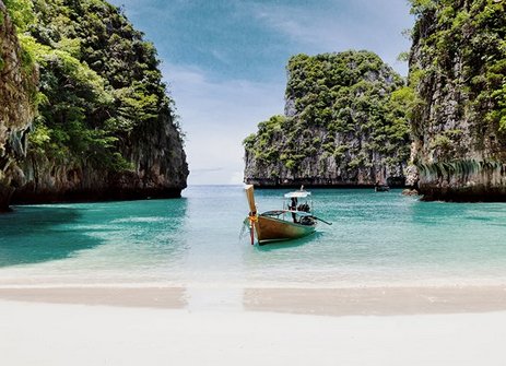 Ein Boot liegt am Strand nahe einer felsigen Küste in Phuket, Thailand, mit Blick auf die Koh Phi Phi Inseln.