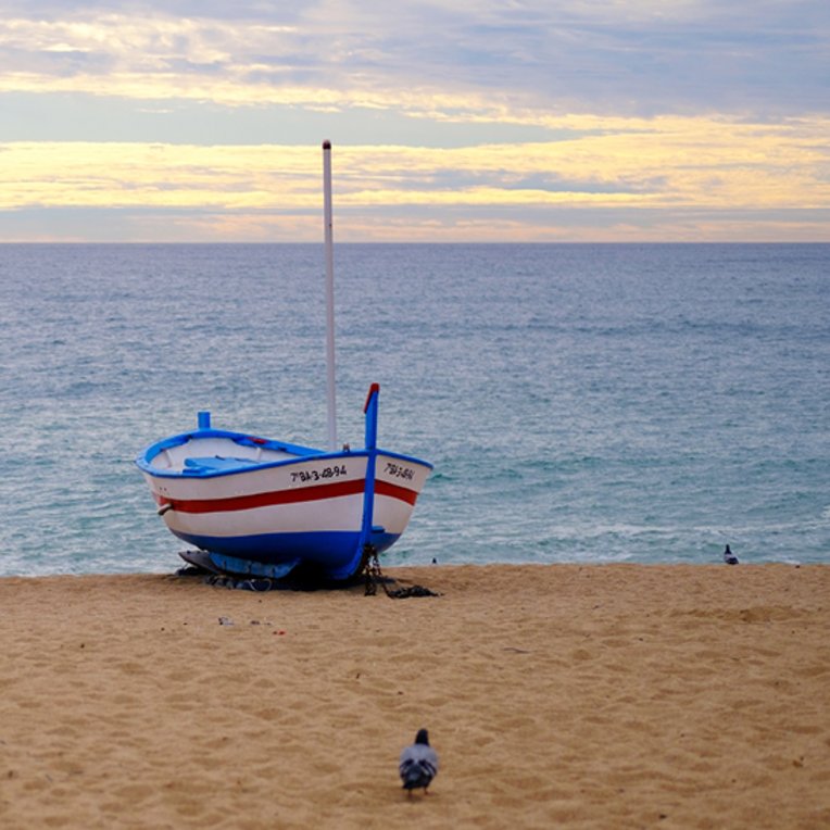 Ein Boot liegt am Strand von Barceloneta in Barcelona, umgeben von feinem Sand und dem blauen Meer.