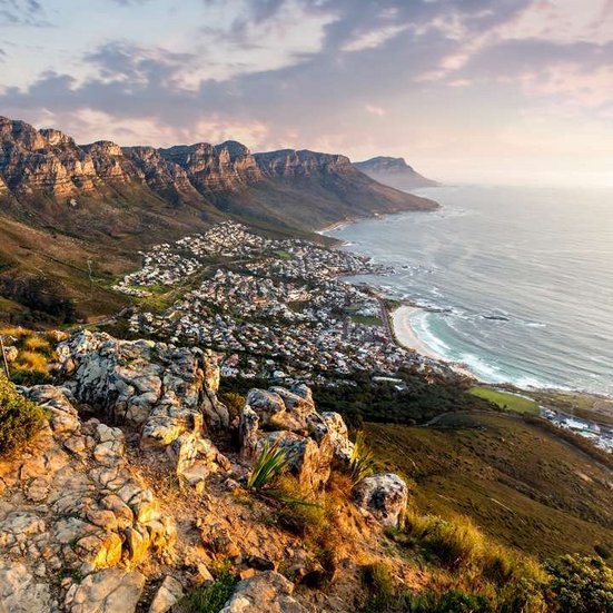 Tafelberg mit Kapstadt im Hintergrund, Südafrika, unter blauem Himmel und grünen Hügeln.