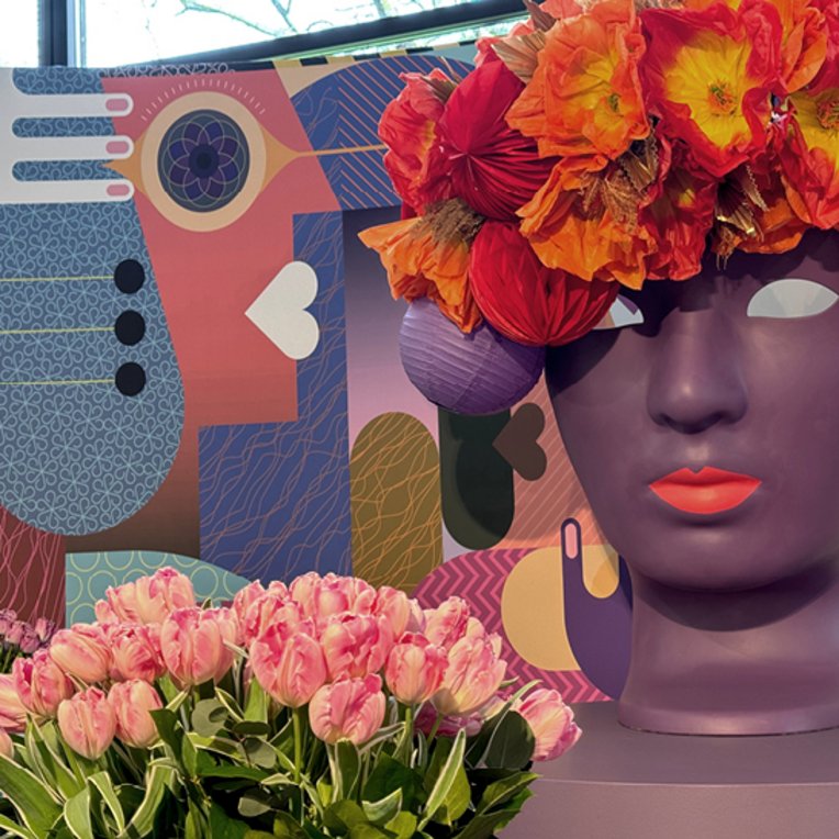 Blumenarrangement auf dem Kopf einer Person in Amsterdam, farbenfroh und kreativ gestaltet.