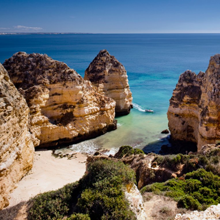 Die Klippen am Strand in Portugal, mit sanften Wellen und klarem Himmel im Hintergrund.