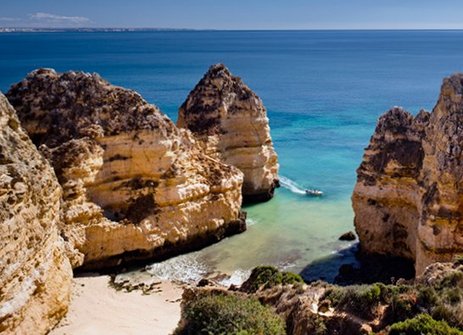 Die Klippen am Strand in Portugal, mit sanften Wellen und klarem Himmel im Hintergrund.