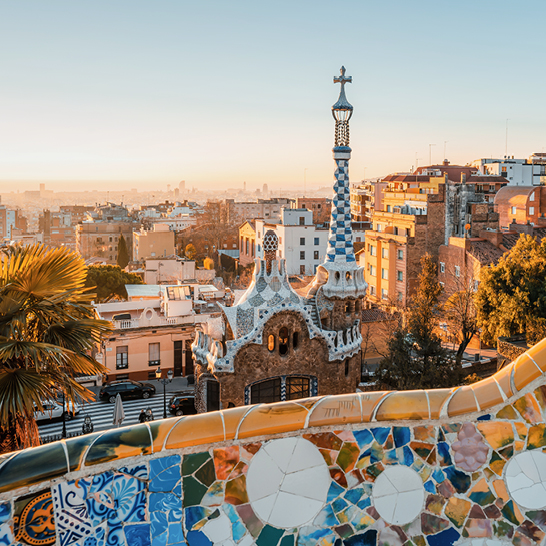 Barcelona bei Sonnenuntergang, mit leuchtenden Farben über der Stadt und silhouettierten Gebäuden im Hintergrund.