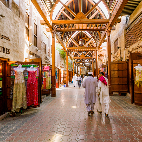 Ein Paar geht entspannt eine Strasse in Dubai entlang, umgeben von modernen Gebäuden und lebhaftem Stadtleben.