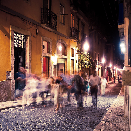 Eine Gruppe von Menschen geht nachts eine gepflasterte Strasse in Lissabon entlang.