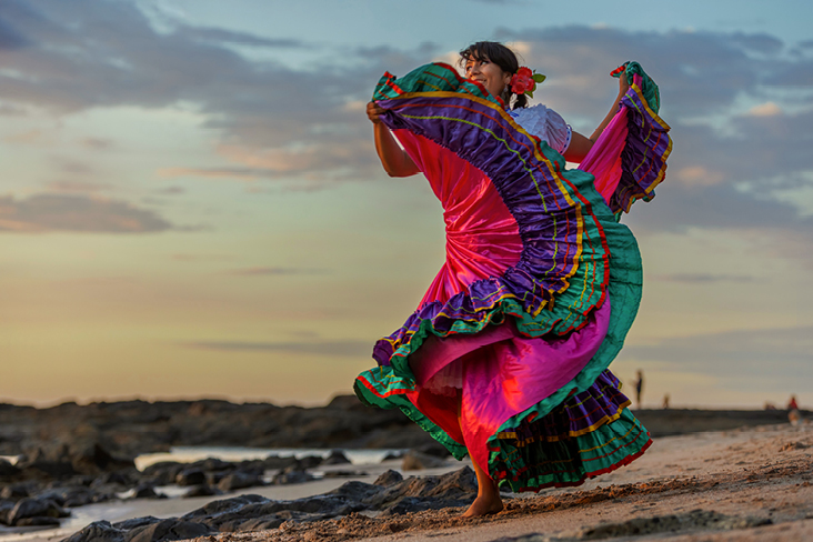 Eine Frau in einem bunten Kleid tanzt fröhlich am Strand in Costa Rica.
