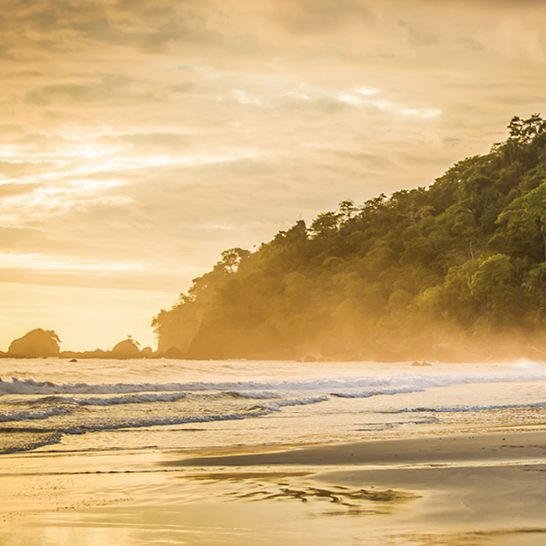 Ein Mann geht am Strand von Manuel Antonio, Costa Rica, mit einem Surfbrett unter dem Arm entlang.