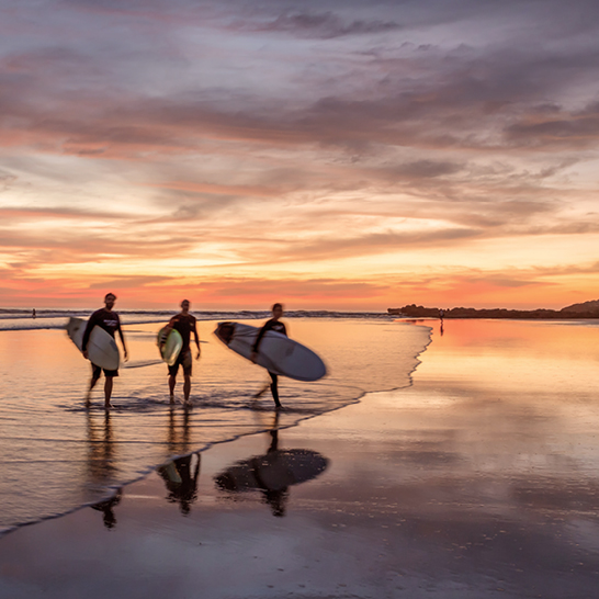 Drei Surfer gehen am Strand bei Sonnenuntergang auf der Nicoya-Halbinsel in Costa Rica.