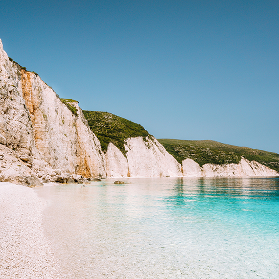 Ein Strand in Griechenland mit klarem blauen Himmel und weißen Klippen im Hintergrund.