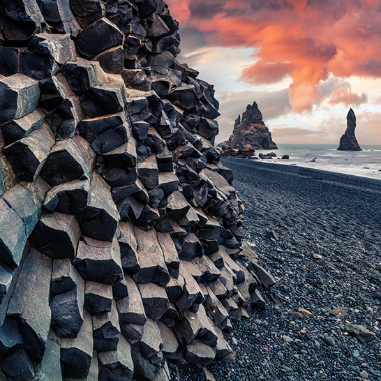 Ein grosser Steinhaufen am Strand von Reynisfjara Island, umgeben von schwarzem Sand und Wellen.