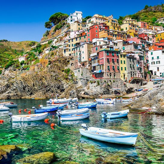 Eine Gruppe von Booten liegt im Wasser, nahe einem bewaldeten Hügel in Cinque Terre, Italien.
