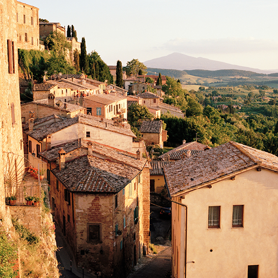  Blick auf ein malerisches italienisches Dorf mit bunten Häusern und sanften Hügeln im Hintergrund.
