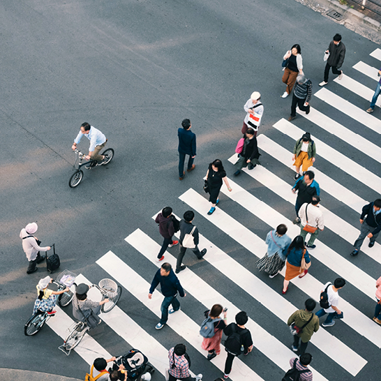 Eine Gruppe von Menschen überquert eine Strasse in Japan, umgeben von modernen Gebäuden und bunten Schildern.