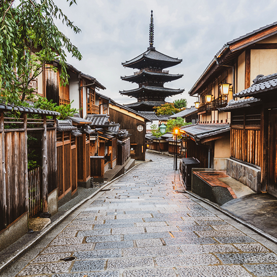 Eine Strasse in Kyoto, Japan, mit einer Pagode im Hintergrund, umgeben von Bäumen und traditionellen Gebäuden.