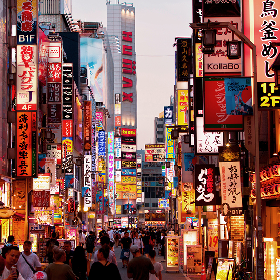Belebte Strasse in Tokio, Japan, mit Menschen, Autos und leuchtenden Reklametafeln.