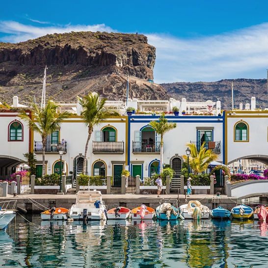 Une rangée de bateaux amarrés dans l'eau, avec en arrière-plan les paysages des Iles Canaries.