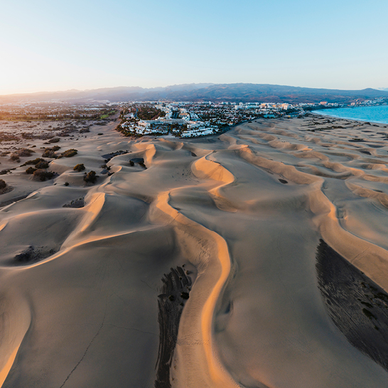 Dunes de sable et plage de Gran Canaria au coucher du soleil, créant une ambiance paisible et colorée.