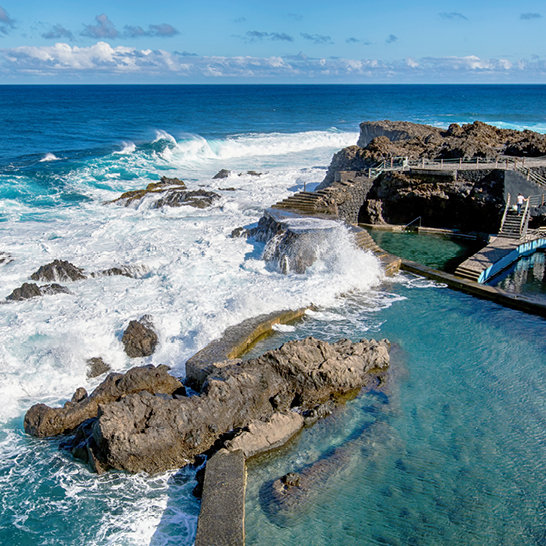 Une grande piscine entourée de rochers et d'eau, avec des palmiers en arrière-plan, créant une ambiance tropicale.