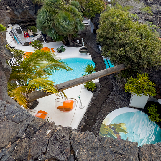 Une piscine entourée de palmiers et de rochers, typique de Lanzarote, évoquant une ambiance tropicale relaxante.