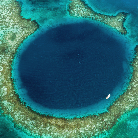 Luftaufnahme eines blauen Lochs im Ozean, umgeben von exotischer Natur und klarem Wasser.