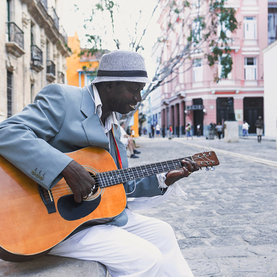 Ein Mann spielt akustische Gitarre an einer Straßenecke und verbreitet karibisches Flair.