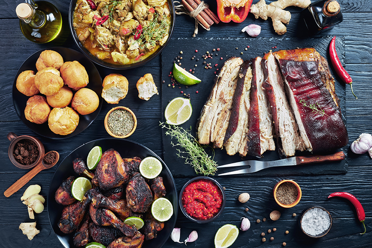 Ein Tisch mit verschiedenen Fleischsorten, Gemüse und Zutaten, inspiriert von der Karibik Kultur.