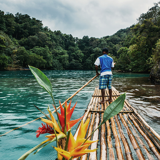 Ein Mann auf einem Bambusfloss in Jamaika, umgeben von klarem Wasser und tropischer Vegetation.