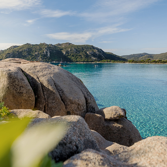 Eine Person sitzt auf einem Felsen und schaut auf ein ruhiges Gewässer.