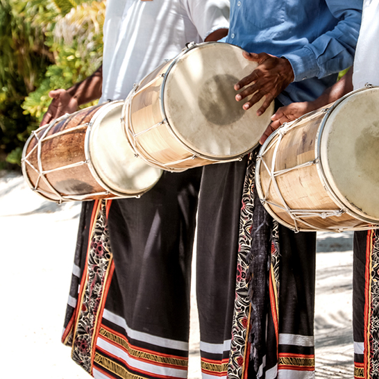 Un groupe d'hommes joue des tambours sur la plage, créant une ambiance festive au bord de l'eau.