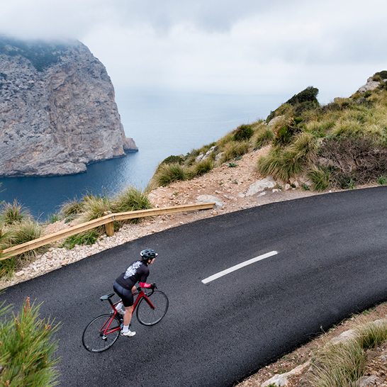 Ein Mann fährt mit dem Fahrrad auf einer Straße in Mallorca, umgeben von der schönen Landschaft der Insel.