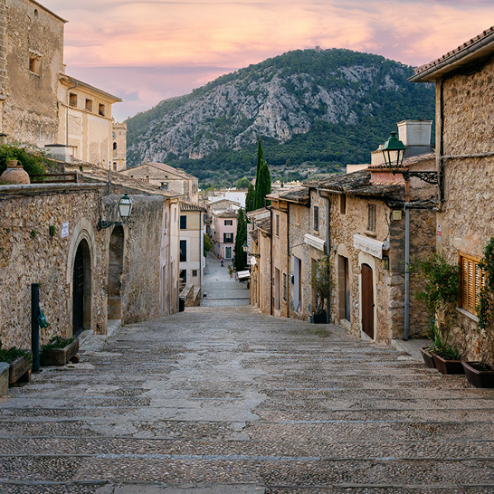 Eine Strasse in Pollensa mit einem markanten Uhrturm in der Mitte, umgeben von charmanten Gebäuden.