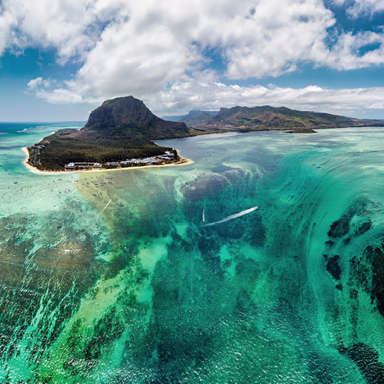 Luftaufnahme eines Riffs und einer Insel vor der Küste von Mauritius, mit klarem Wasser und bunten Korallen.