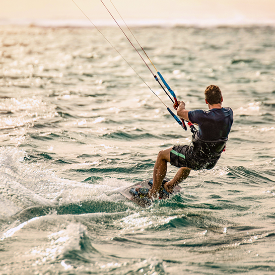 Un homme fait du windsurfing dans l'océan à l'île Maurice, avec des vagues et un ciel ensoleillé en arrière-plan.
