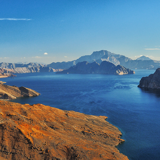 Weitläufiges Wasser mit majestätischen Bergen im Hintergrund, die Fjorde Arabiens in Oman zeigen.