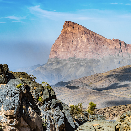 Jebel Shams in Oman mit einer beeindruckenden Felsformation im Hintergrund, umgeben von majestätischen Bergen.
